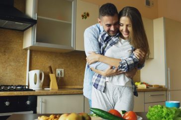 Happy young couple embracing and talking in the kitchen while cooking breakfast at home in the morning
