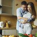 Happy young couple embracing and talking in the kitchen while cooking breakfast at home in the morning