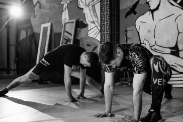 Two men stretching inside a gym, preparing for MMA training in a grayscale setting.